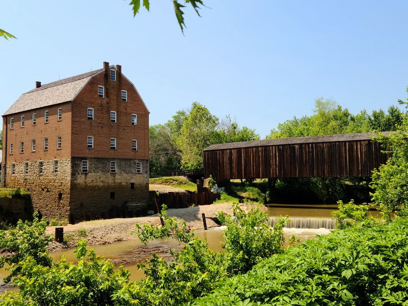 A Stone Mill And Covered Bridge Sharing One Riverbank